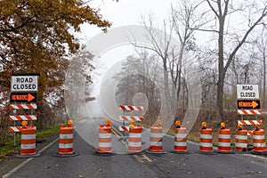 Road closed detour signs at a barricaded road disappearing into dense for, transportation these landscape