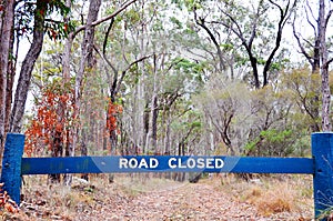 Road closed sign blocking vehicles on gravel dirt of bush forest