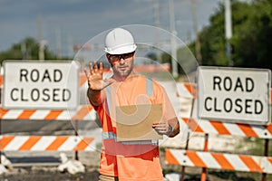 Road closed. Road worker outdoor. Builder in a hard hat working on a construction project at a site. A builder worker in