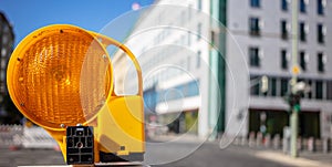 Road construction concept. Orange reflector caution light. Blur city background, space, banner