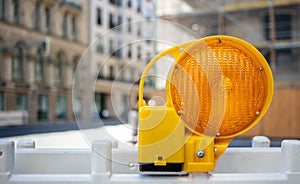 Road construction concept. Orange reflector caution light. Blur city background, space