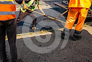 Road construction crew used shovels to scatter more asphalt over the top of the new pavement. At road construction site