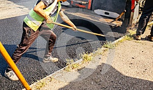 Road construction crew used shovels to scatter more asphalt over the top of the new pavement. At road construction site