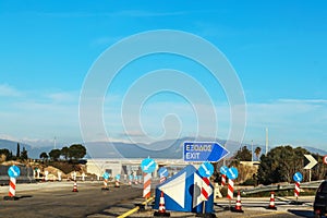 Road construction in Greece with an Exit sign in Greek and English and lots of road direction signs under an overpass and