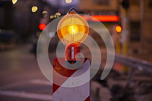Road construction sign light in orange on a red and white stand