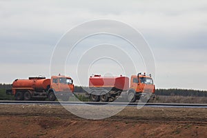 Road construction work - two red watering trucks at highway among field