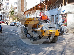 Road construction worker driving between parking cars on the narrow street.