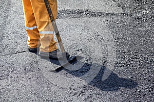 Road construction worker leveling fresh asphalt pavement