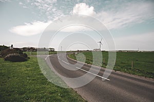 Road at the countryside of Kirkwall, Scotland with residential Building and modern wind turbine at the horizon