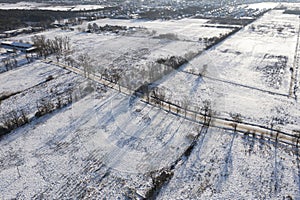 A road covered with snow among fields and meadows, view from a drone