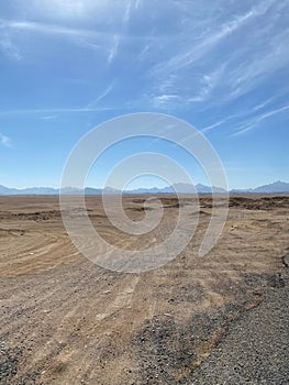 Buggy tracks. Road in the desert. Mountains on the horizon. Light clouds.