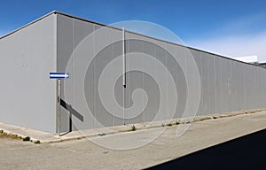 Road directional arrow sign at the corner of a gray concrete block building. Sidewalk and asphalt road in front