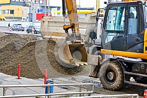 Road excavator works on the sidewalk and loads sand onto the truck