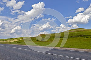 Road in the field, long distance trail in the field. Beautiful green hills. Blue sky with fluffy clouds