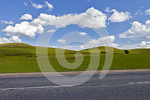 Road in the field, long distance trail in the field. Beautiful green hills. Blue sky with fluffy clouds