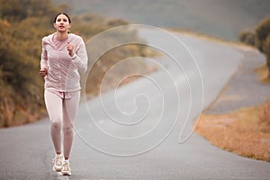 Road, fitness and woman running for exercise in nature for race, competition or marathon training. Challenge, sports and