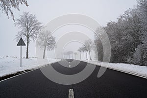 Road on a foggy winter day in the landscape with snow and trees on the sides