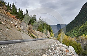 Road in the forest. A rocky slope with fir trees on one side and a mountain river on the other.