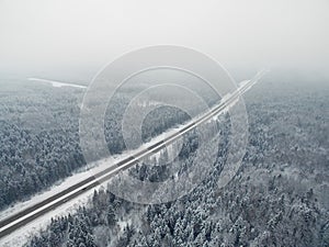 Road in the frozen winter forest with driving cars. Foggy vanishing point perspective. Aerial