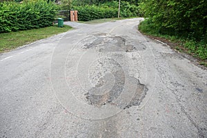 The road is full of holes and potholes. The old asphalt road surface is rough and bumpy and in need of repair.