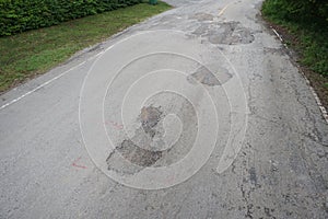 The road is full of holes and potholes. The old asphalt road surface is rough and bumpy and in need of repair.