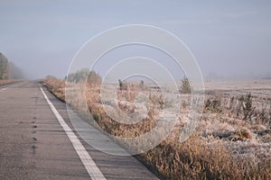 The road goes into the distance into the fog. Rime on grass