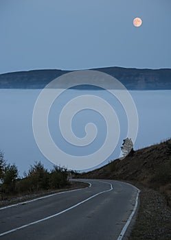 The road goes down into the clouds and fog in the mountains and the orange moon in the sky