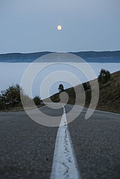 The road goes down into the clouds and fog in the mountains and the orange moon in the sky