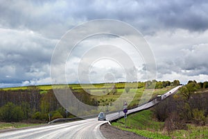 Road goes far away into the distance, horizon, few cars, green field and forest, cloudy blue sky background