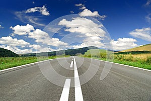 Road among green fields, blue sky and white clouds above