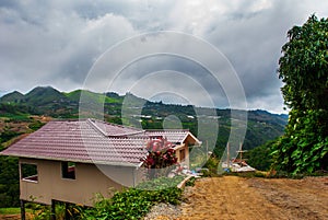 The road and houses in the village on the slopes of the mountains with clouds. Sabah, Borneo, Malaysia