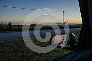 Road from the inside of a car and the reflection of the rear-view mirror of the car. road trip at sunset