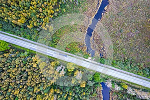 road intersecting blue river among autumn yellow forests, bogs