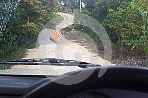 Road through jungle, view behind windshield of car. Dangerous upward climb