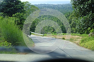 Road through jungle, view behind windshield of car. Palm trees and sea in background