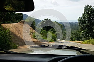 Road through jungle, view behind windshield of car. Palm trees and sea in background