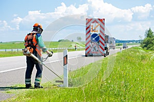 Road landscapers cutting grass around mileposts