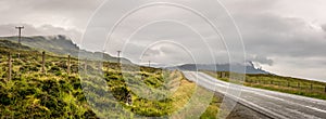 A road leading into the distance with the old man of storr in the background, silhouetted. gray, grey clouds gathering around the