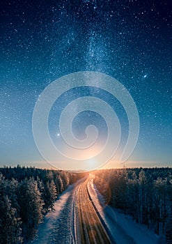 Road leading towards sunset and stars of the milky way through snowy boreal forest. Transportation and epic landscapes