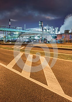 Road markings with oil refinery on background at night