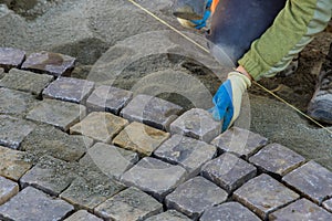 Road master of gloves lays paving stones in layers stone road by professional worker using hammer