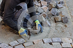 Road master in gloves lays paving stones in layers stone road by professional worker using stones and hammer