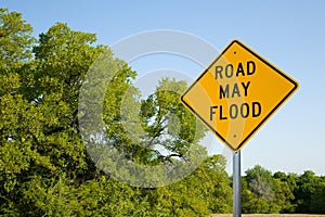 Road May Flood Sign In Spring With Green Trees And Clear Blue Sky