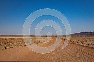 Road meandering through expansive desert landscape with distant mountain range in Namibia, Luderitz