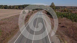 Road and moving cars between colorful autumn forest in Ural