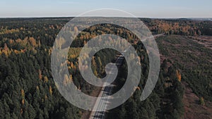 Road and moving cars between colorful autumn forest in Ural