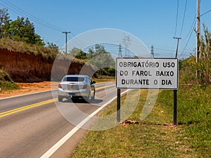 Road with a new traffic sign informing the new law that requires the use of headlights on even during the day on the roads with a