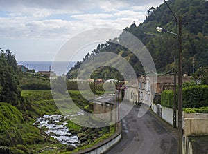 Road in old small village Faial da Terra with cascading river and sea horizon, Sao Miguel, Azores
