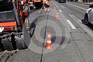 Road orange cones enclose the work crew and road equipment from the carriageway