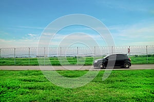 Road Outside Airport Lined by a Wire Fence with green grass and black car